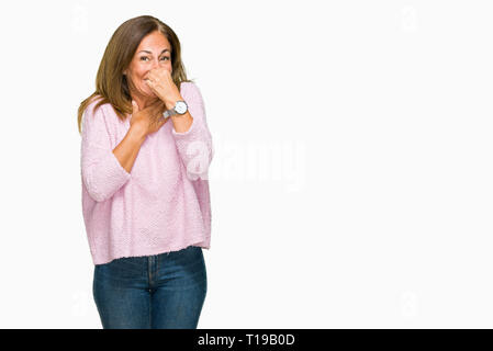 Beautiful middle age adult woman wearing winter sweater over isolated background smelling something stinky and disgusting, intolerable smell, holding  Stock Photo