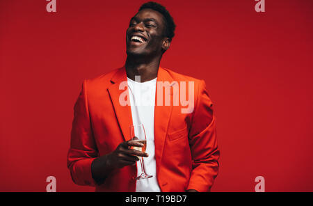 Handsome young african man with a glass of champagne. Smiling young guy having champagne against red background. Stock Photo