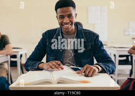Smiling male student in college classroom with books. Teenage boy sitting in college classroom. Stock Photo