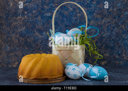 Easter bread and painted Easter eggs in a basket on dark stone table Stock Photo