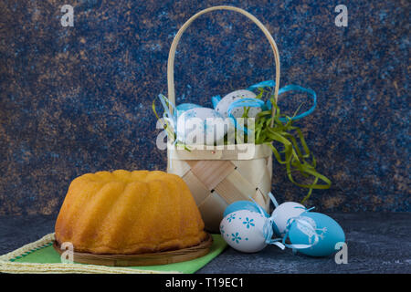 Easter bread and painted Easter eggs in a basket on dark stone table Stock Photo