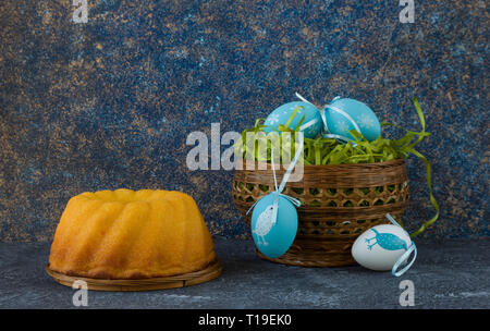 Easter bread and painted Easter eggs in a basket on dark stone table Stock Photo