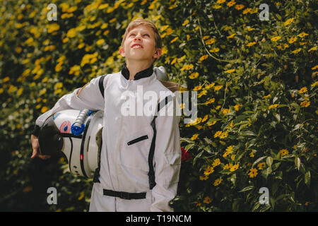 Boy in space suit with helmet walking outdoors and looking up. Cute boy in space suit and helmet playing astronaut outdoors. Stock Photo