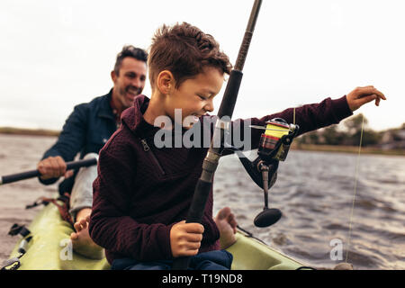 Kid fishing in lake with his father. Kid releasing the thread tied to the fishing rod in the lake to catch fish. Stock Photo