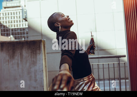 Side view of african woman leaning to a railing with soft drink bottle. Woman enjoying on her weekend. Stock Photo
