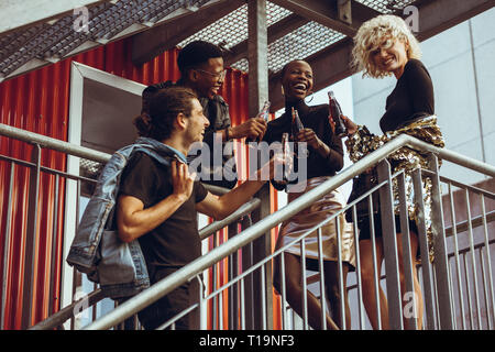 Group of young friends hanging out on weekend. Multiracial men and women standing on steps having soft drinks. Stock Photo