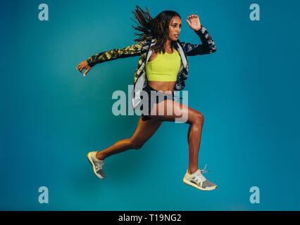 Full length shot of fitness woman running over blue background. Hispanic female model doing running exercise. Stock Photo