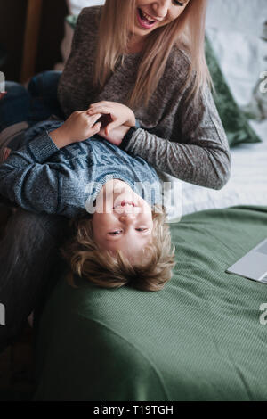 Cheerful little boy having fun with mother on sofa