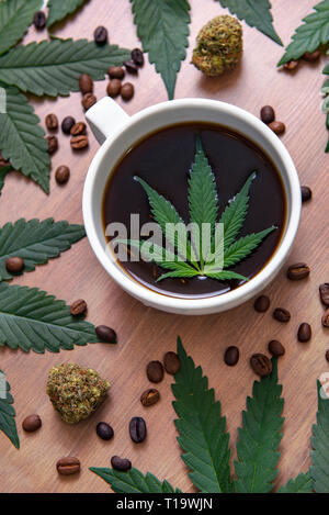 Coffee cup and cannabis with beans, nugs and marijuana leaves over wood background, marijuana edibles concept Stock Photo