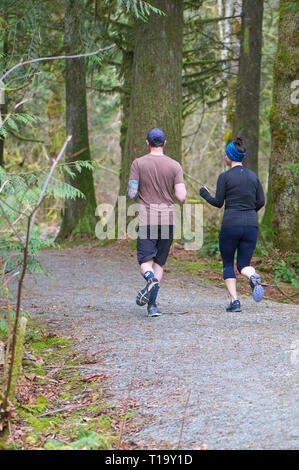 Young couple running on a trail in a forested area of Cliff Falls Park, Maple Ridge, B. C. Stock Photo