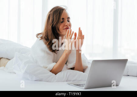 Young woman doing video call on laptop and speaking hand language on bed in light room Stock Photo