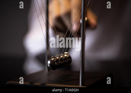 Unrecognizable blurred male pulling ball of metal Newton cradle and observing momentum Stock Photo