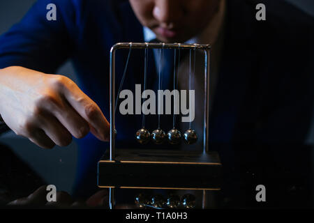 Unrecognizable businessman pulling small metal ball of Newton cradle and observing momentum over glass tabletop Stock Photo