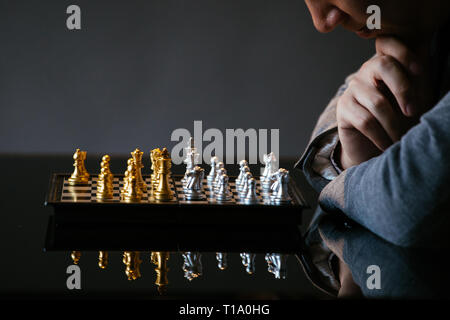 Cropped shot of man rubbing chin and thinking over next move while playing chess at glass table on gray background Stock Photo
