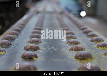 A rusty metal railing of a bridge with a multitude of bolts on top of it Stock Photo