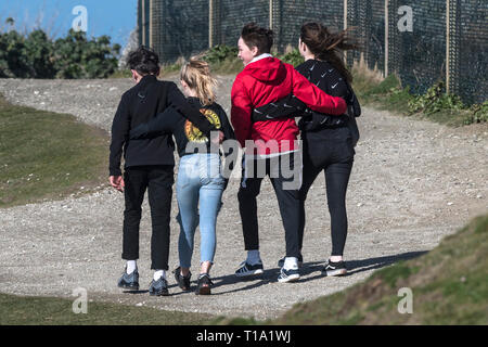 Young teenagers with their arms around each other looking out to sea. Stock Photo