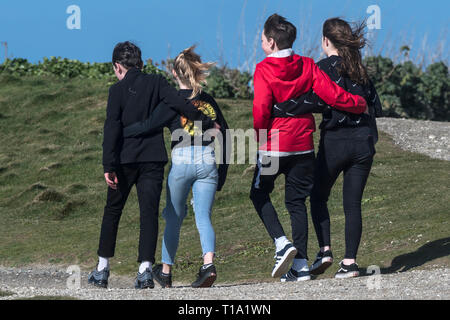 Young teenagers with their arms around each other walking along a footpath. Stock Photo