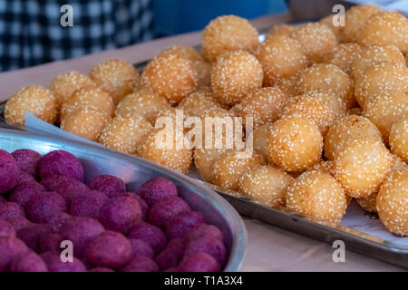 Thai traditional dessert. Deep fried sesame balls and deep fried sweet potato balls on stainless steel tray of seller. Purple and brown sweets balls. Stock Photo