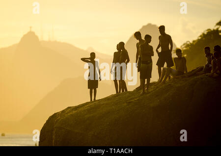 RIO DE JANEIRO - MARCH 4, 2017: Young Brazilians gather on a large rock preparing to jump into the sea at Niteroi, across Guanabara Bay from Corcovado Stock Photo