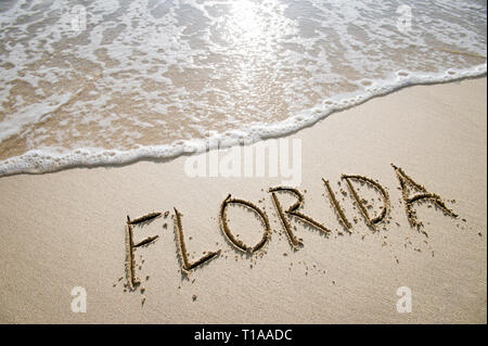 Simple Florida American holiday getaway message written in smooth sand with an incoming wave on a tropical beach Stock Photo