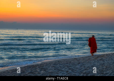 This great photo shows the sunrise of Hua Hin in Thailand early morning at sunrise. On the beach you can see a Buddhist monk walking Stock Photo