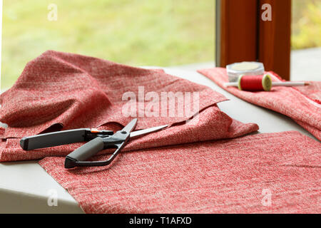 Home sewing crafts projects hobbies. Cloth fabric, scissors, and thread on table. Stock Photo