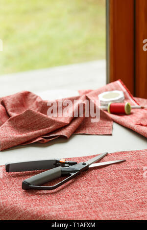 Home sewing crafts projects hobbies. Cloth fabric, scissors, and thread on table. Stock Photo