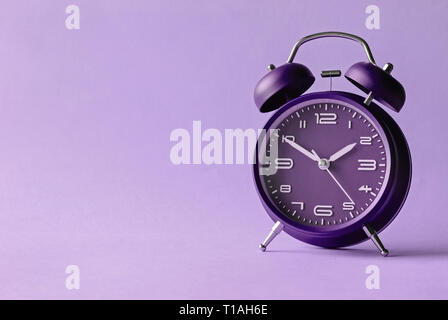 Old fashioned red alarm clock with bells centered over a violet background with lateral copy space Stock Photo