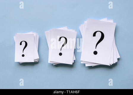 Three piles of question marks printed on white paper in different sizes arranged in a row on a blue background in a conceptual image Stock Photo