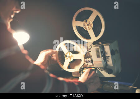 man set up film reel on vintage 8mm movie projector in dark room Stock Photo