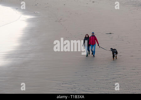 Bournemouth, Dorset, UK. 25th Mar 2019. UK weather: after a lovely sunny day, the day finishes with a golden sunset at Bournemouth beach, as visitors head to the seaside to enjoy the last rays of sun and watch the sun go down. Couple walking their Bernese Mountain dog along the seashore. Stock Photo