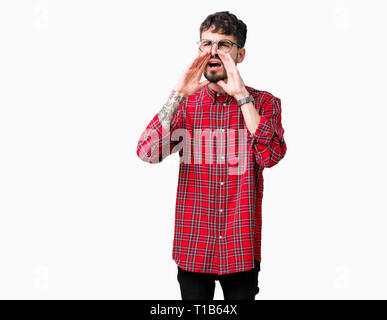 Young handsome man wearing glasses over isolated background Shouting angry out loud with hands over mouth Stock Photo