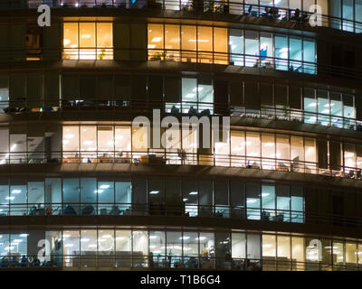 Window of the multi-storey building of glass office lighting and working people within. Windows office building for background. People working late Stock Photo