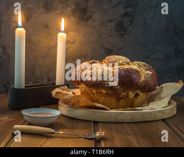 Sweet Challah bread on a wooded round plate on wooden brown table with honey and two candles on Shabbat evening making Kidush / black background with Stock Photo