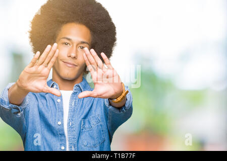 Young african american man with afro hair Smiling doing frame using hands palms and fingers, camera perspective Stock Photo