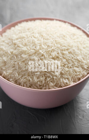 Dry white rice basmati in a pink bowl over concrete background, side view. Close-up. Stock Photo