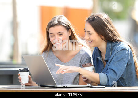 Two happy friends checking online content on laptop sitting in a park Stock Photo