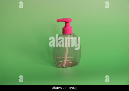 One red plastic bottle on a green background. Bottle for cosmetics with dispenser. There are no inscriptions on the bottle. No labels. Stock Photo