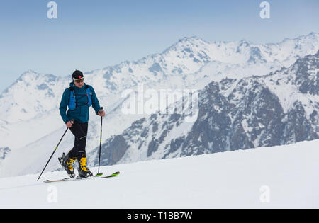 Mountaineer backcountry ski walking up along a snowy ridge with skis in the backpack. In background blue sky and shiny sun and Zebru, Ortler in South Stock Photo