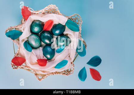 Easter background with eggs decorated in blue, turquoise and gold in nest with colorful feathers. Top view. Copy space. Stock Photo