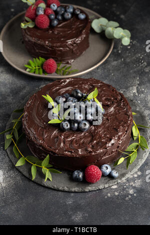 Chocolate cakes with berries and green leafs on gray plate, fresh raspberry and blueberry near on dark background. Concept of holiday dessert Stock Photo