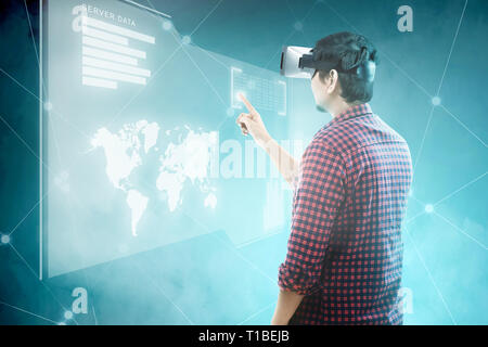 Rear view of asian man touching binary code on digital interface with virtual reality device display the world map, graphic bar and binary code. Augme Stock Photo