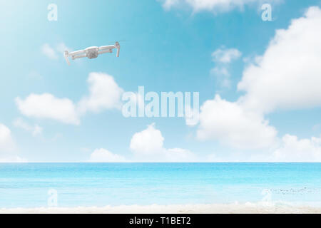 White drone with camera flying over the beach with blue ocean and blue sky background Stock Photo