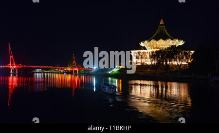 Scenic night view of illuminated State Legislative Assembly and pedestrian bridge. Boat walk by Sarawak river. Waterfront landmarks in Kota Kuching. Stock Photo