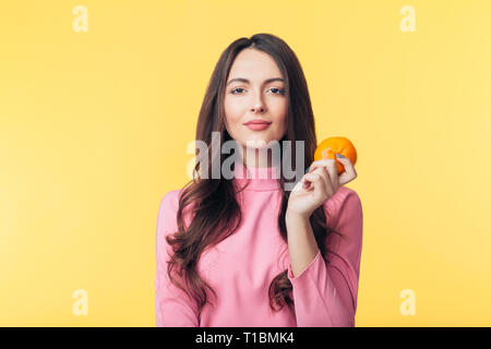 Beautiful young woman holding orange in hand isolated on yellow background. Healthy food concept Stock Photo