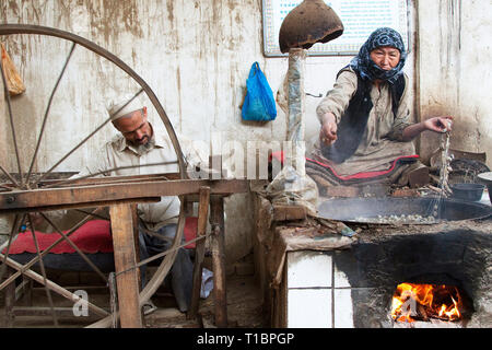 Old technique of spinning silk. Silk worm cocoons are boiled in a large pot and stirred with a stick, 'cooked,' strands from 10 or 12 cocoons are join Stock Photo