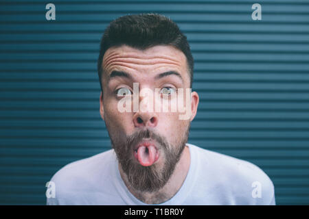 Portrait of bearded man looking on camera and hsowing his tongue. Guys brows are raised up. Isolated on striped and black background. Stock Photo