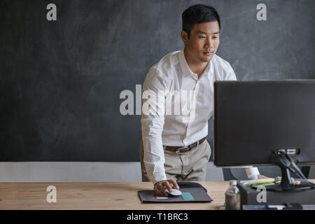 Asian businessman standing at his desk working on a computer Stock Photo
