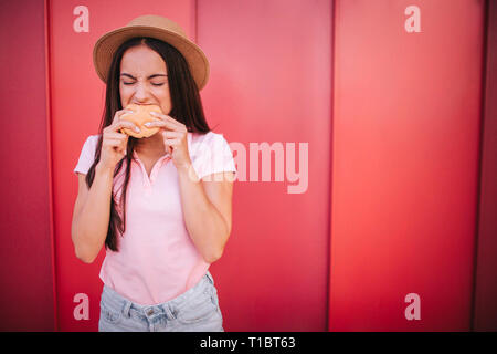 A picture of girl stands and bites a piece froom roll. She holds it with both hands. Woman is keeping her eyes closed. She is concentrated. Isolated Stock Photo