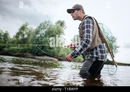 https://l450v.alamy.com/450v/t1bwyp/fisherman-in-action-he-stands-in-water-and-holds-fly-rod-in-one-hand-and-spoon-in-the-other-one-also-adult-has-a-fishing-net-on-the-back-green-t1bwyp.jpg